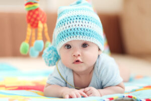 little child lying on a children's rug in the white-blue cap