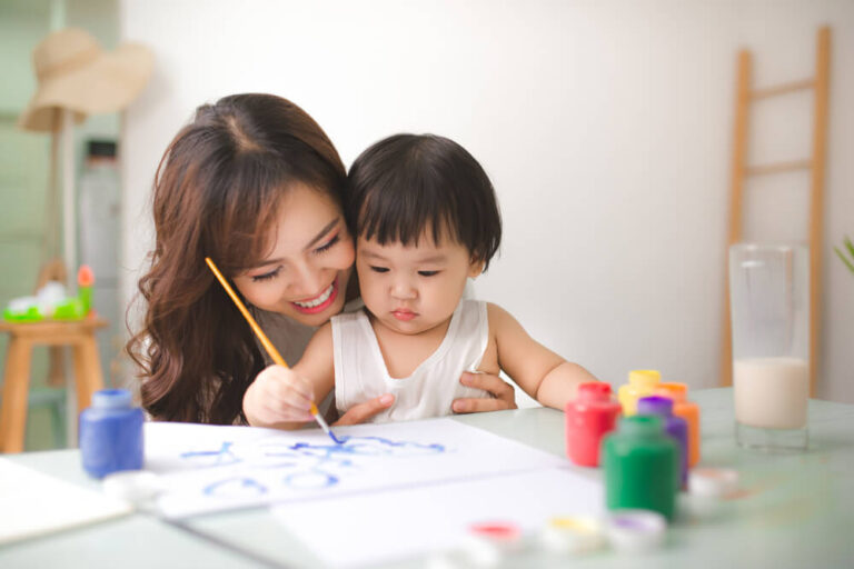 Happy woman helps her child girl with painting
